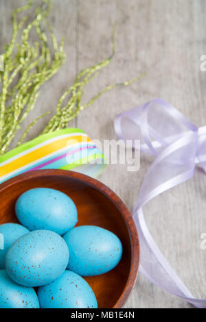 Eine hölzerne Schüssel voller Blau gesprenkelt Eier von Pastelltönen Bänder auf einem rustikalen graue Tabelle umgeben Stockfoto