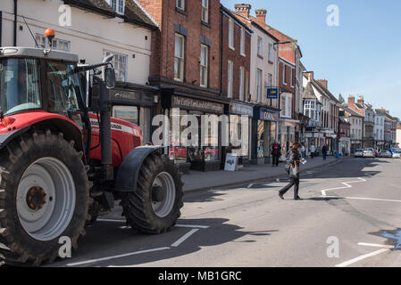 Eine Frau kreuzt die Straße in Newport, Shropshire, während ein Farmer Traktor wartet geduldig auf Ihr der Straße in der Sonne Kreuz Stockfoto