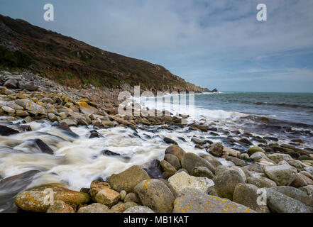 Einen schönen und stimmungsvollen Küsten Szene im Larmorna Cove in der Nähe von Penzance und Mousehole in West Cornwall mit Wasser nach unten Kaskadieren von den Bergen zum Meer Stockfoto