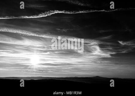 Sonnenuntergang über die Berge in der Ferne, mit tiefen Himmel voller Wolken und Kondensstreifen Stockfoto