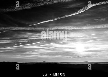 Sonnenuntergang über die Berge in der Ferne, mit tiefen Himmel voller Wolken und Kondensstreifen Stockfoto