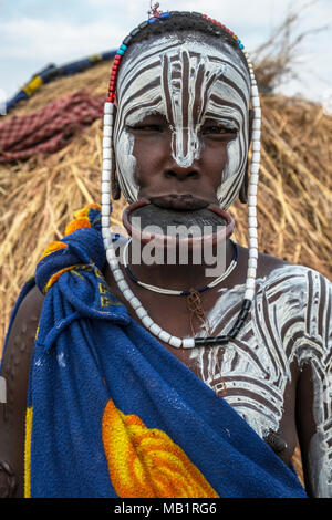 Omorate, Äthiopien - Januar 24, 2018: Porträt einer unbekannten Frau aus Mursi Stamm mit einem großen Lippe Platte in ihrem Dorf mit traditionellen Häusern. Stockfoto