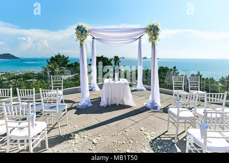 Der Hochzeit Setup auf dem Hügel mit Panoramablick auf das Meer, weiße Chiavari Stühle mit Konus von Rosen Blütenblatt, der Bogen und Altar in Weiß dekoriert Stockfoto