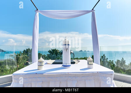 Die Hochzeit Bogen, Altar setup mit weißer Tisch, der eine große und zwei kleine Kerze verwenden für die Dekoration auf dem weißen Tisch mit Stoffbezug. Die Ehe Stockfoto
