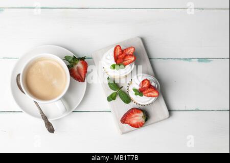 Vanille Cupcakes mit Erdbeere und Tasse Kaffee auf einem hellen Hintergrund Stockfoto