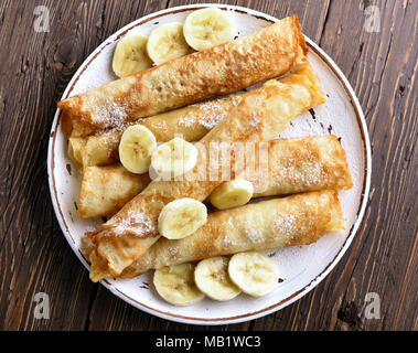 Nahaufnahme von Crepes Rolle mit bananenscheiben auf Holz- Hintergrund. Ansicht von oben, flach Stockfoto