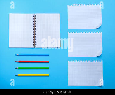 Weiße leere Blatt, aus einem Notebook mit Bohrungen und Bunte Bleistifte aus Holz auf einem blauen Hintergrund Stockfoto