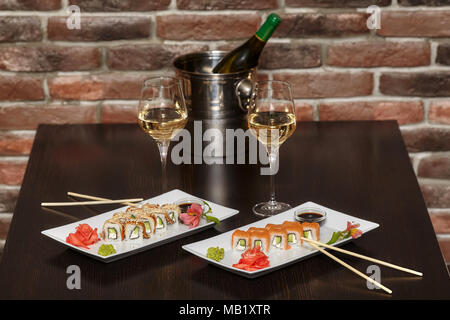 Zwei Sätze von sushi Rollen auf weiße Platte mit Stäbchen und Weingläser Stockfoto