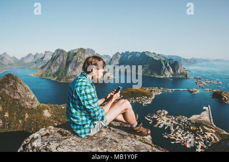 Mann Reisender mit Smartphone sitzen auf Berge Seitenanfang Reisen lifestyle Konzept Abenteuer outdoor Reinebringen Berg Luftaufnahme Lofoten Stockfoto