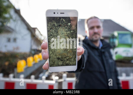 04 April 2018, Deutschland, Paderborn: Stefan Werth zeigt ein Foto auf sein Smartphone der Bombe auf seinem Grundstück gefunden. Ein 1,8 Tonnen britisches dud war nur 80 cm U-Bahn während der Gartenarbeit gefunden. 26 000 Bewohner in einem 1 km Radius um die Bombe haben ihre Häuser für die Deaktivierung zu verlassen. Die Stadt plant, die größte Evakuierung in der Geschichte. Foto: Friso Gentsch/dpa Stockfoto