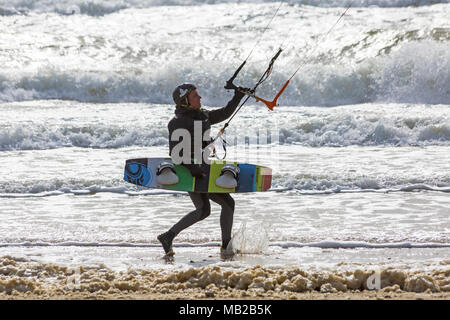 Sandbanks, Poole, Dorset, Großbritannien. April 2018. UK Wetter: Luftiger Tag in Sandbanks, wenn Kitesurfer das Beste aus den windigen Bedingungen machen. Kitesurfer tragen Kiteboard in Richtung Meer. Kitesurfer Kitesurfer Kitesurfer Kitesurfer Kitesurfer Kitesurfer Kitesurfen Kitesurfen Kitesurfen Kitesurfen Kitesurfen Kitesurfen Kitesurfen Kitesurfen Kitesurfen Kitesurfen Stockfoto