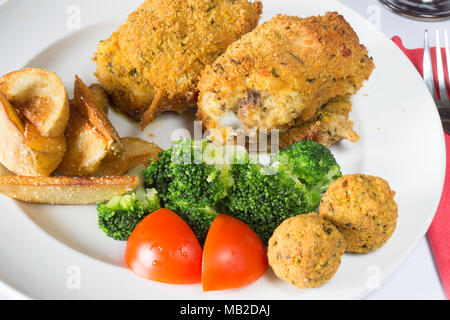 Ein englisches Pub/Restaurant Teller Golden gebratene panierte Hühnerkeule mit Kartoffelecken serviert, Brokkoli und Füllung Kugeln Stockfoto