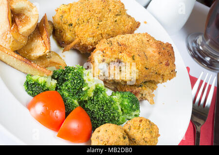Ein englisches Pub/Restaurant Teller Golden gebratene panierte Hühnerkeule mit Kartoffelecken serviert, Brokkoli und Füllung Kugeln Stockfoto