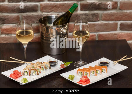 Zwei Sätze von sushi Rollen auf weiße Platte mit Stäbchen und Weingläser Stockfoto