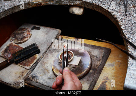 Der Juwelier hält ein gefrorenes Stück geschmolzene Gold mit einer Pinzette. Stockfoto