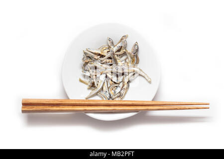 Japanische getrocknet Kleinkind Sardine mit hölzernen Eßstäbchen isoliert auf weißem backgroung. Japanische Küche. Gesunde Snack essen. Iriko niboshi oder Fisch. Stockfoto