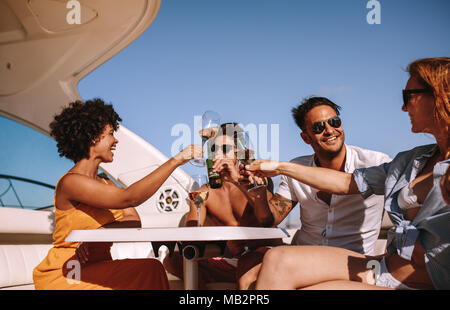 Gruppe von jungen Männern und Frauen an der Rückseite des Bootes sitzen und toasten Getränke. Junge Leute Party auf einem Boot mit Getränken. Stockfoto