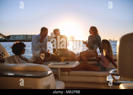 Junge reiche Freunde trinken Wein und Bier in Boot Partei während des Sonnenuntergangs. Gruppe von Jugendlichen feiern auf der Yacht. Stockfoto