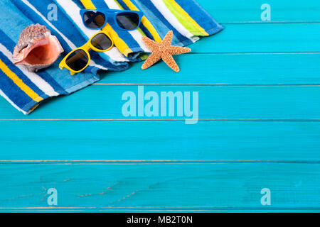 Beach Szene mit gestreiften Handtuch, Sonnenbrille, Seesterne und seashell auf alten verwitterten blau lackierten Holz Belag. Platz für Kopieren. Stockfoto