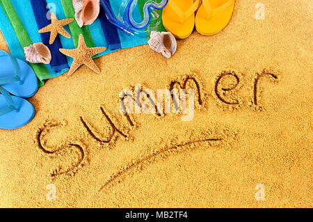 Das Wort Sommer auf einem Sandstrand geschrieben, mit dem Scuba Mask, Strandtuch, Seesterne und Flip Flops Stockfoto