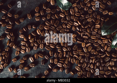 Blick von oben auf die schäbigen Tabelle mit dem Lügen geröstete Kaffeebohnen im Chaos mit grünen Blättern. Stockfoto