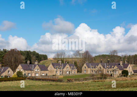 Reihe traditioneller Steinhäuser in einem ländlichen britischen Dorf, unter einem blauen Himmel mit Wolken, umgeben von grünen Feldern und Wäldern Stockfoto