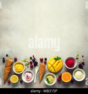 Draufsicht Rot, Rosa, Gelb, Grün, Weiß Eis Kugeln in Schalen, Waffeln, Beeren, Orange, Mango, Pistazie, grauer Beton Hintergrund. Bunte Stockfoto