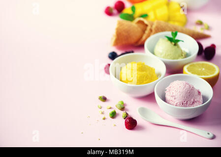 Rot, violett, gelb, grün, weiß Eis Kugeln in Schalen, Waffeln, Beeren, Orange, Mango, Zitrone, Minze, Pistazie, Rosa shabby chic Hintergrund. Stockfoto