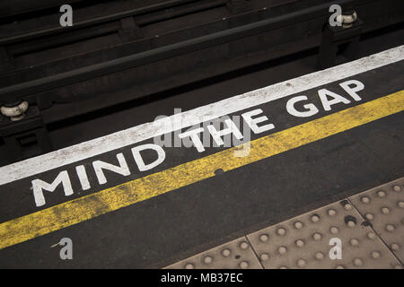 Die Lücke Rohr Plattform Warnschild auf einer Londoner U-Bahn-Station in London, Vereinigtes Königreich. Mind the gap ist ein akustisches oder optisches Warnsignal Phrase auf Fahrgäste zu Vorsicht beim Überqueren der horizontalen, und in einigen Fällen vertikale Abstand zwischen der Tür und dem Bahnsteig. Stockfoto