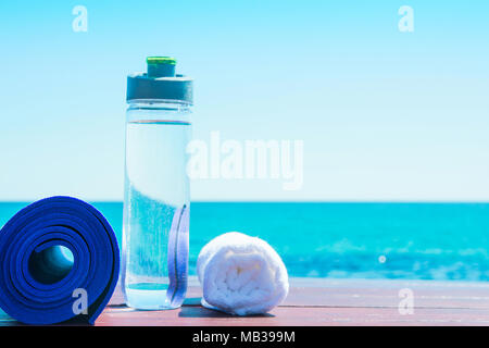 Yoga Matte rollte die Flasche mit Wasser Weiß Handtuch am Strand mit türkisblauem Meer blauer Himmel im Hintergrund. Sonnenlicht. Entspannung Sommer Meditation Fitness Wellb Stockfoto