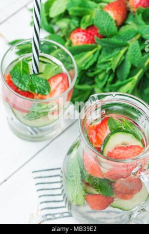 Frische kühle infundiert Detox Wasser mit Reifen Erdbeeren in Scheiben geschnittene Gurken Minze im Glas- und Kanne. Weiß Plank Holz Hintergrund. Gesundes Getränk Detox Stockfoto