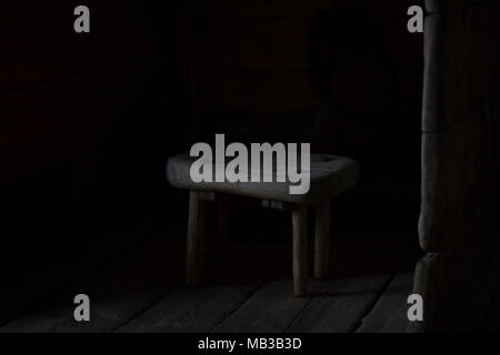 Hocker, allein in einem hölzernen Scheune - mit Licht aus ein einsames Fenster und Schatten hinter sich. Stockfoto