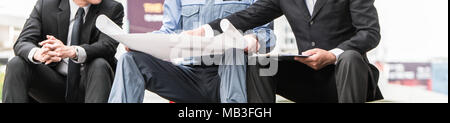 Ingenieure treffen auf der Terrasse auf der Baustelle. Mitarbeiter diskutieren. Chef und Arbeitnehmer streiten. Gespräch in Team. tragen Helm halten Papier pla Stockfoto