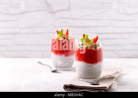 Gesunde Chia, Kokos, Erdbeere Pudding mit hausgemachtem Müsli auf weissem Holztisch Stockfoto