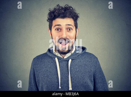 Junger Mann mit grosses Lächeln und lassen Sie sich überraschen auf grauem Hintergrund posiert. Stockfoto