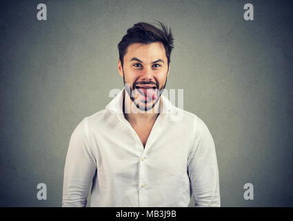 Junge legerer Mann im weißen Hemd, Gesicht und Zunge an Kamera und Witz. Stockfoto