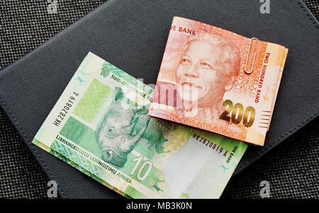 Wad von 200 und 10 Rand Währung Banknoten aus Südafrika auf ein graues Leder Hintergrund Stockfoto