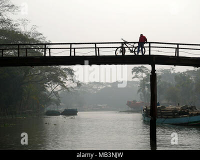 Mann mit Fahrrad auf die Brücke in die backwaters Bereich gesehen. Im Delta der Flüsse Ganga (Padma), Brahmaputra und Meghna Menschen leben auf dem Wasser. Bereich rund um die Stadt Banaripara mit Wasser geflutet wird. Die Menschen leben in Dörfern am Ufer des Flusses. Kein Straßenverkehr ist möglich. Nur Wasser und Schiffe verbinden Sie mit dem Rest der Welt. Aber die Gegend ist sehr lebhaft. Die Landwirte beim Anbau von Obst, Gemüse, Reis und Getreide auf 2 700 Quadratkilometer Land unter den Fluss. Anbieter besuchen ihre Kunden auf Booten. Schwimmende Märkte mit Gemüse, Obst, Reis oder Holz sind in diesem sind Stockfoto