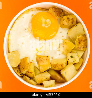 Spiegelei mit Bratkartoffeln Frühstück in einer Schüssel gegen einen orangen Hintergrund Stockfoto