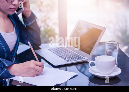 Asian Business Frau Aufruf mit dem Schreiben auf Papier schreiben, Thai Büro Frau mit Bleistift und das Telefon beantworten, schönes Büro in Büro- und Stockfoto