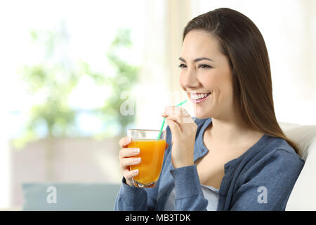 Happy girl Holding einen Orangensaft Glas auf einer Couch im Wohnzimmer zu Hause sitzen Stockfoto