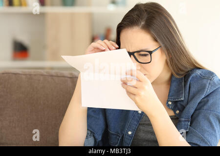 Frau mit Augen Probleme auf einen Buchstaben auf einer Couch im Wohnzimmer zu Hause sitzen Lesen Stockfoto