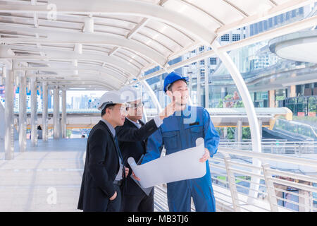 Ingenieure treffen auf der Terrasse auf der Baustelle. Mitarbeiter diskutieren. Chef und Arbeitnehmer streiten. Gespräch in Team. tragen Helm halten Papier pla Stockfoto