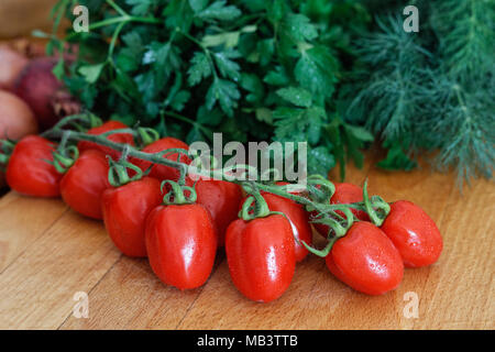 Traube-Tomate Rebe auf Holz Schneidebrett vor einem Haufen frischer Dill und Petersilie. Stockfoto