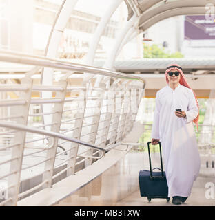 Araber in Travel Concept. Junge saudi-arabischen Mann in traditioneller Kleidung wandern mit Koffer am Flughafen Hintergrund Stockfoto