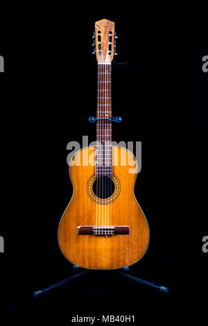 Sehr alte Gitarre auf einem Ständer auf schwarzem Hintergrund Stockfoto
