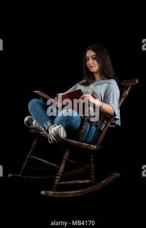 Junges Mädchen mit einem Buch in einen Schaukelstuhl, auf schwarzem Hintergrund Stockfoto