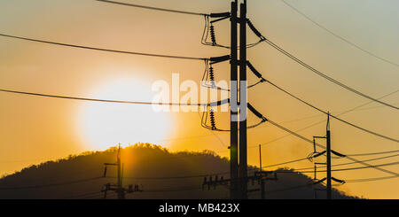 Hochspannung Strommasten und Leitungen (Silhouette) mit Sonnenuntergang im Hintergrund. Low Key, in der Nähe. Natürliche (Sonne) und industrielle Quellen von Energie zusammen Stockfoto