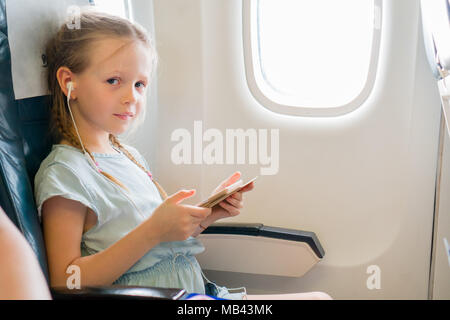 Adorable kleine Mädchen von einem Flugzeug reisen. Cute kid mit Laptop in der Nähe der Fenster in Flugzeugen Stockfoto