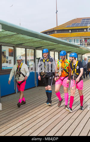 Bournemouth, Dorset, Großbritannien. 7. April 2018. UK Wetter: Nach einem feuchten Start in den Tag die Sonne versucht, heraus zu kommen, obwohl es auf der kühlen Seite Besucher gehen nach Bournemouth Strand am Meer während der Osterferien zu genießen. Die hellen und farbenfrohen, einer Gruppe junger Männer auf einem Junggesellenabschied für eine Fahrt auf dem Drahtseil gekleidet Stockfoto